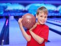 Little smiling boy dressed in red T-shirt holds ball in bowling club